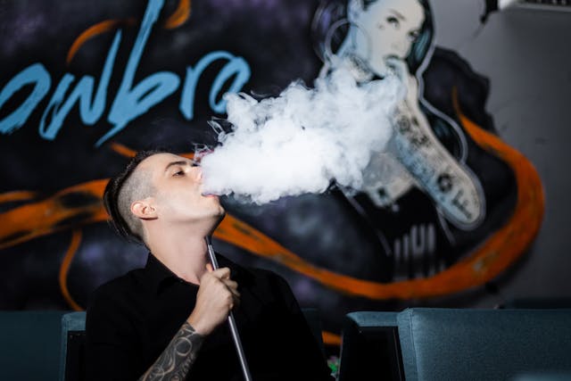 a tattooed man blowing a vape cloud